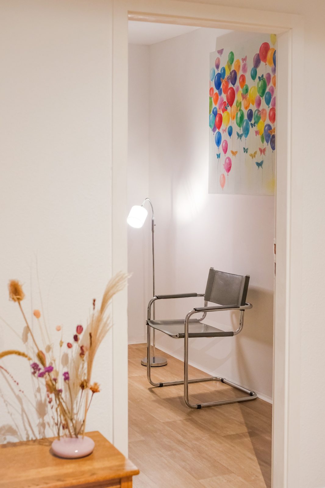 Blick in einen hellen Praxisraum mit Stuhl, Stehlampe und buntem Bild